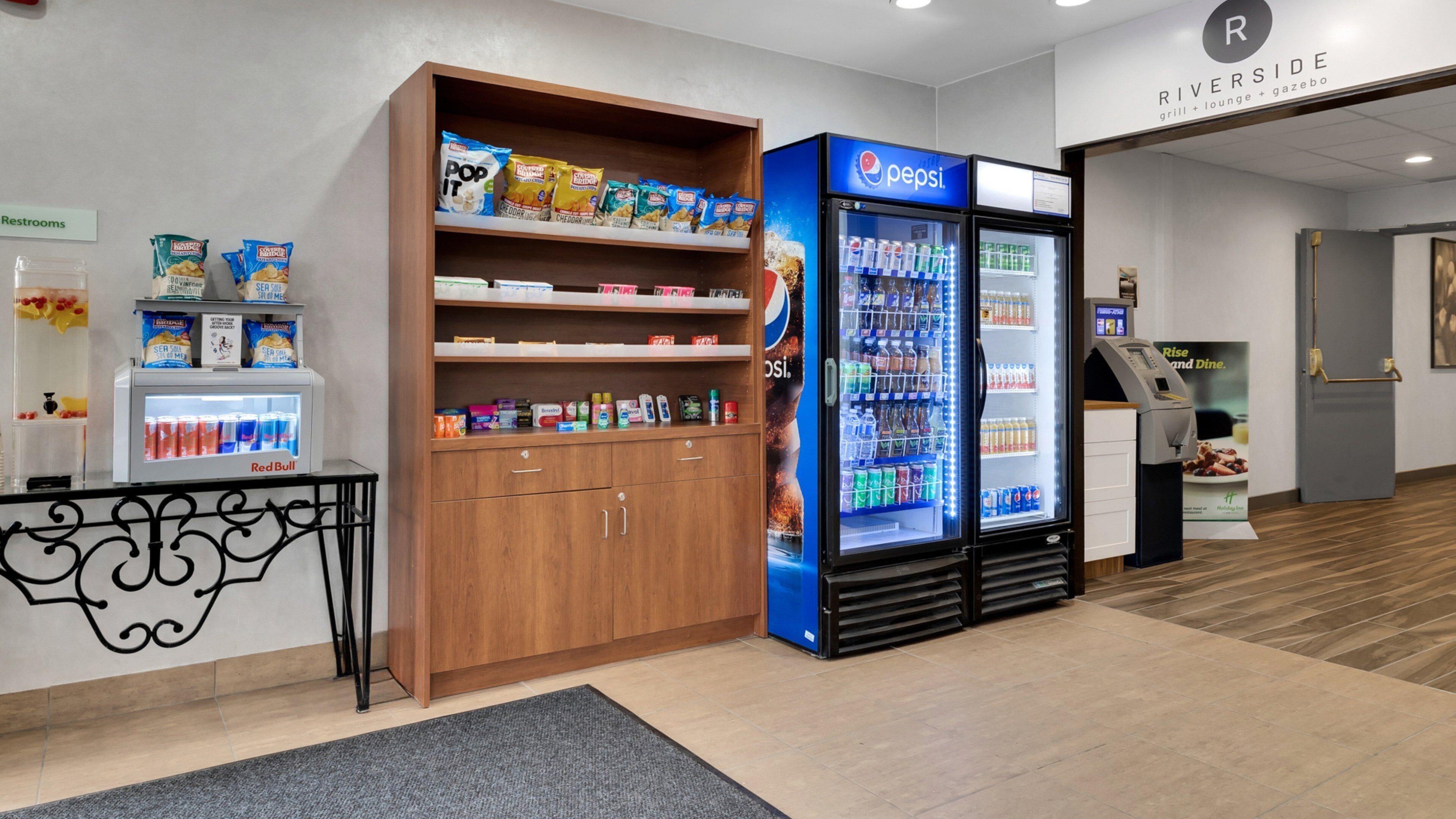 A vending machine stocked with snacks and beverages, a refrigerator with drinks, and a small table with a drink cooler.