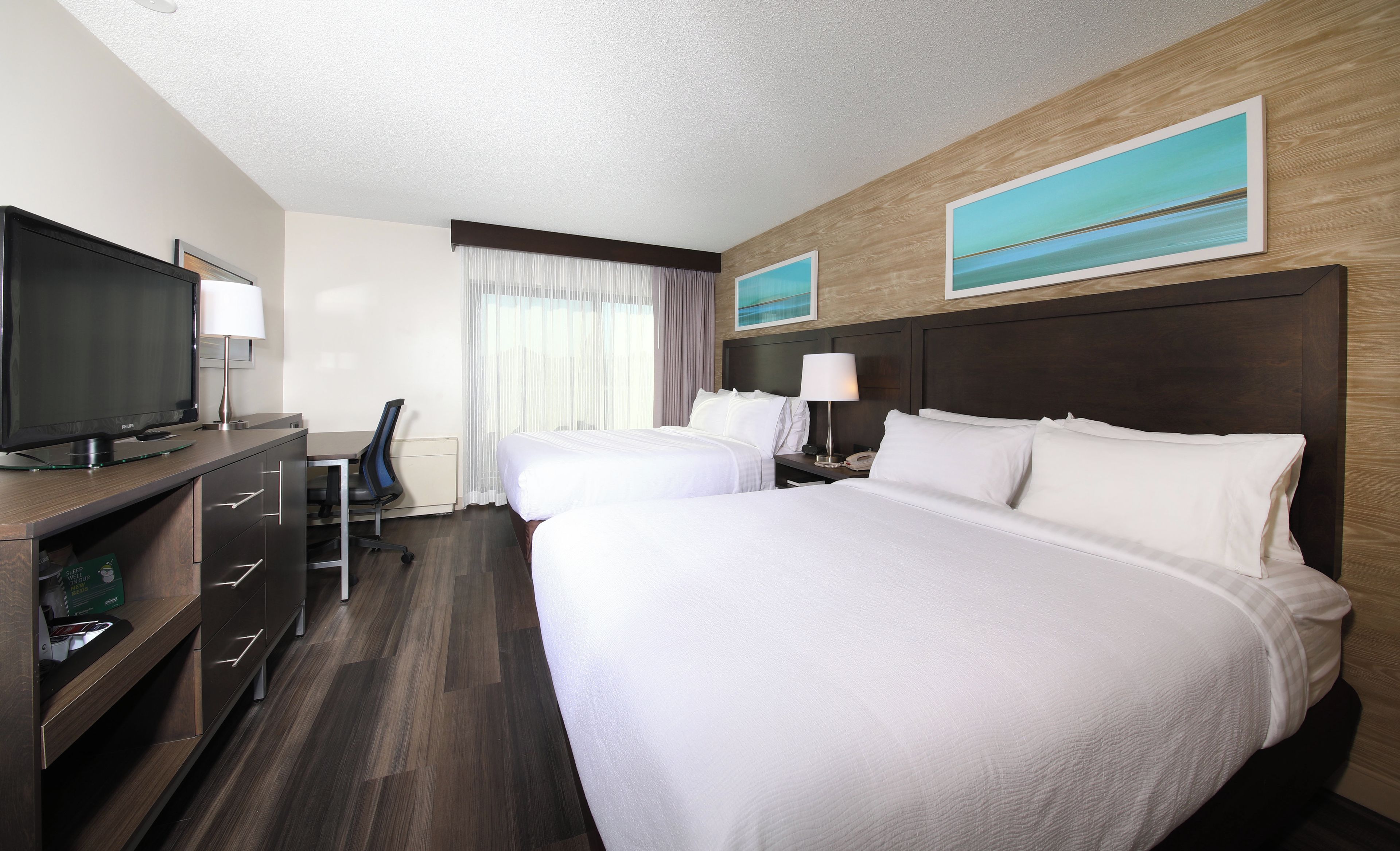 Habitación de hotel con cama, escritorio, computadora, televisor y ventana con cortinas.
