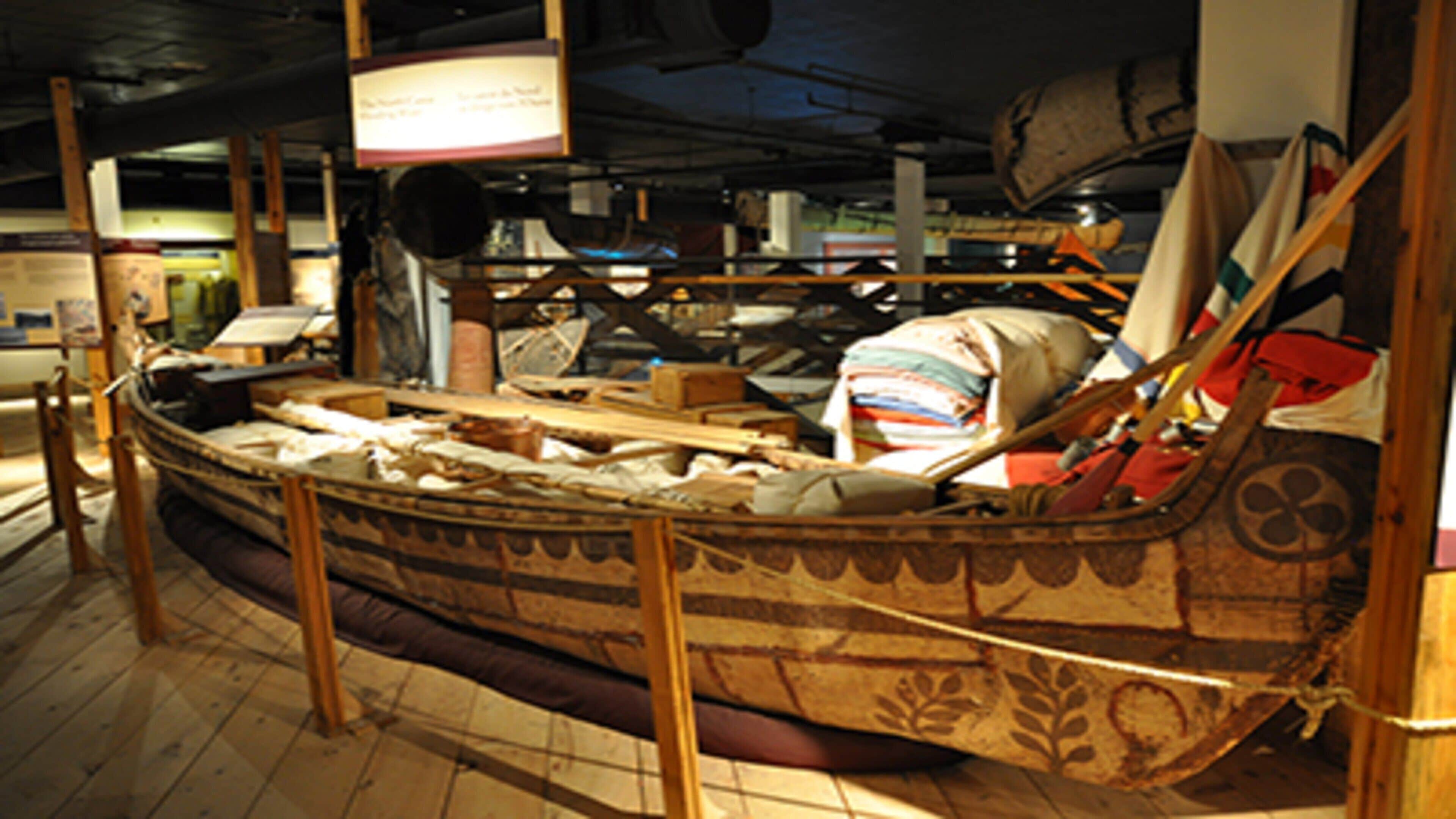 Una habitación con forma de barco, suelo de madera, un banco y varios objetos expuestos.