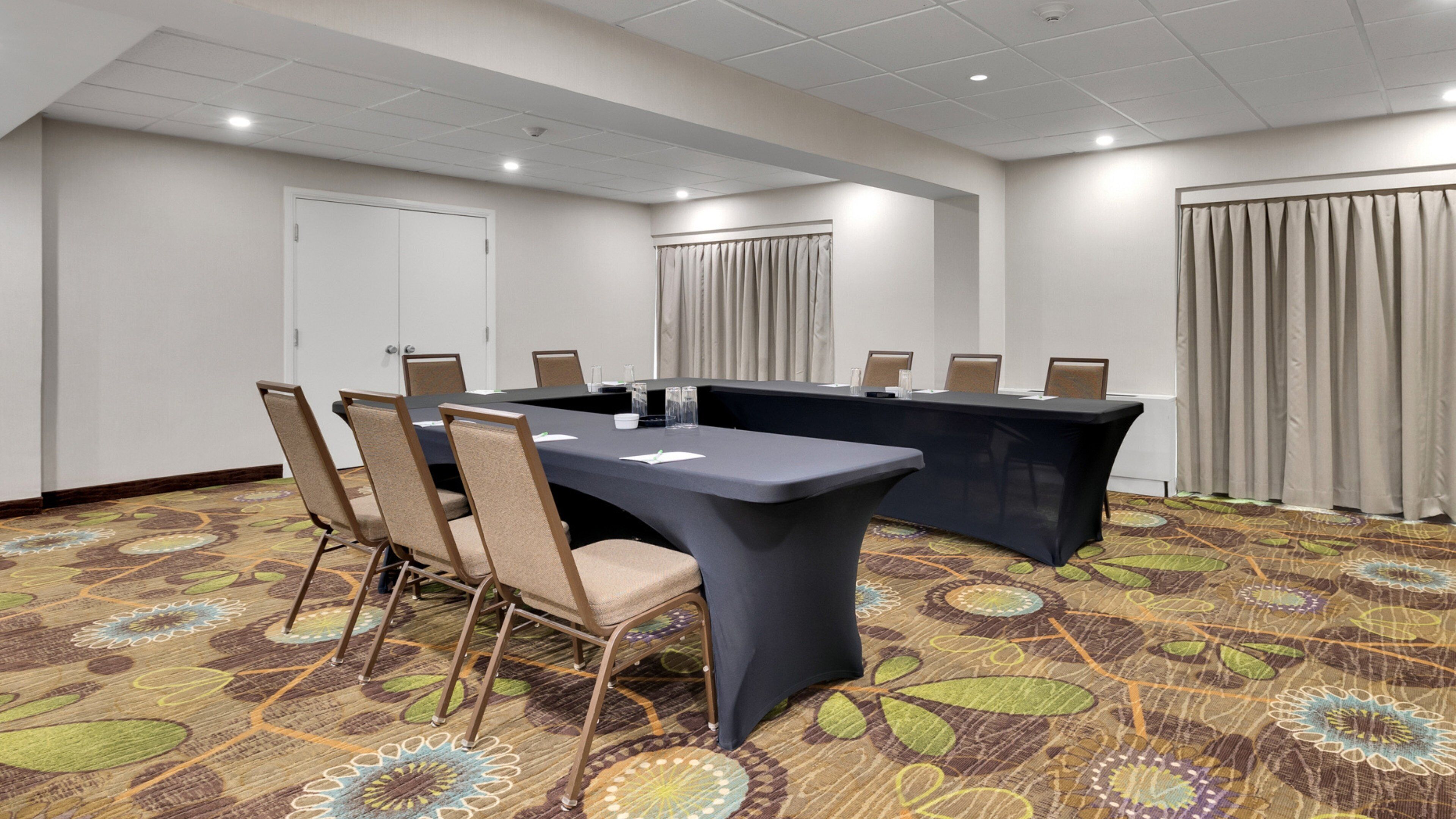Una sala de conferencias con una mesa grande, sillas, una barra y cortinas.