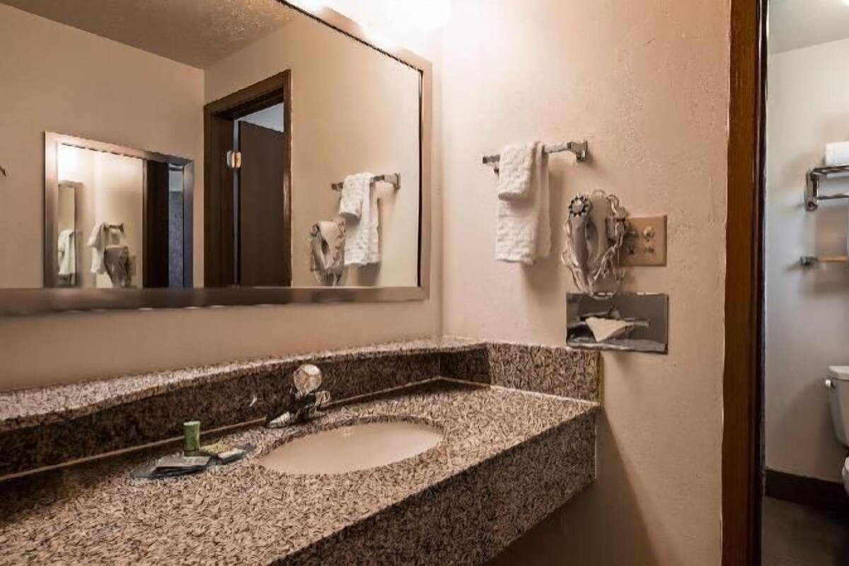 A bathroom with a granite countertop, two sinks, a mirror, a towel rack, and a toilet.