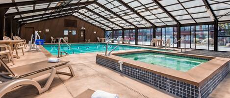Una piscina interior con techo de cristal, sillones de descanso y un jacuzzi.