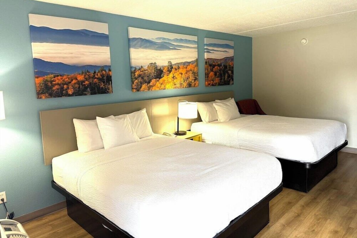 A hotel room with two beds, a nightstand, and three paintings on the wall.