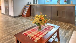 A reception area with a wooden reception desk, a vase of flowers, a checkered placemat, and a blue wall with a 'Days Inn' sign. - Days Inn by Wyndham Harriman (Harriman)
