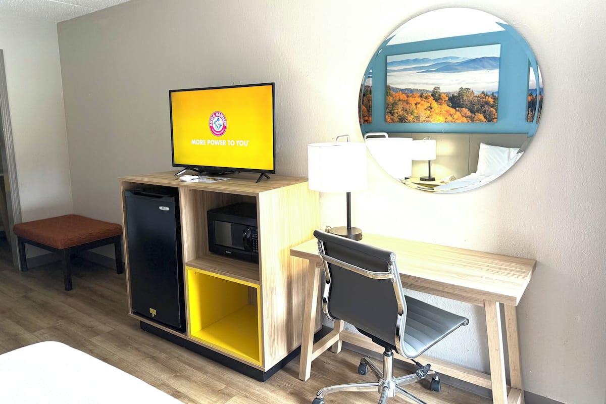A hotel room with a desk, chair, television, and a mirror.