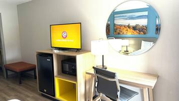 A hotel room with a desk, chair, television, and a mirror.