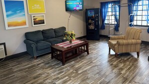 A living room with a dark green sofa, a wooden coffee table with a vase of flowers, a flat-screen TV mounted on the wall, and a vending machine. - Days Inn by Wyndham Harriman (Harriman)