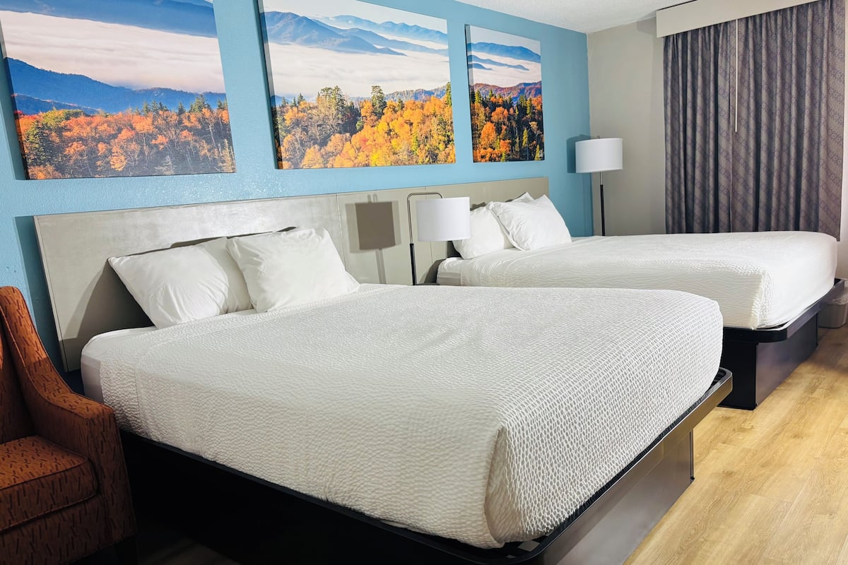 A hotel room with two beds, a wooden chair, and three large landscape paintings on the wall.