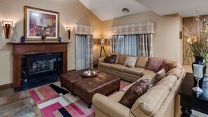 A living room with a fireplace, a sofa, an ottoman, and a coffee table. - Best Western Lapeer Inn (Lapeer)