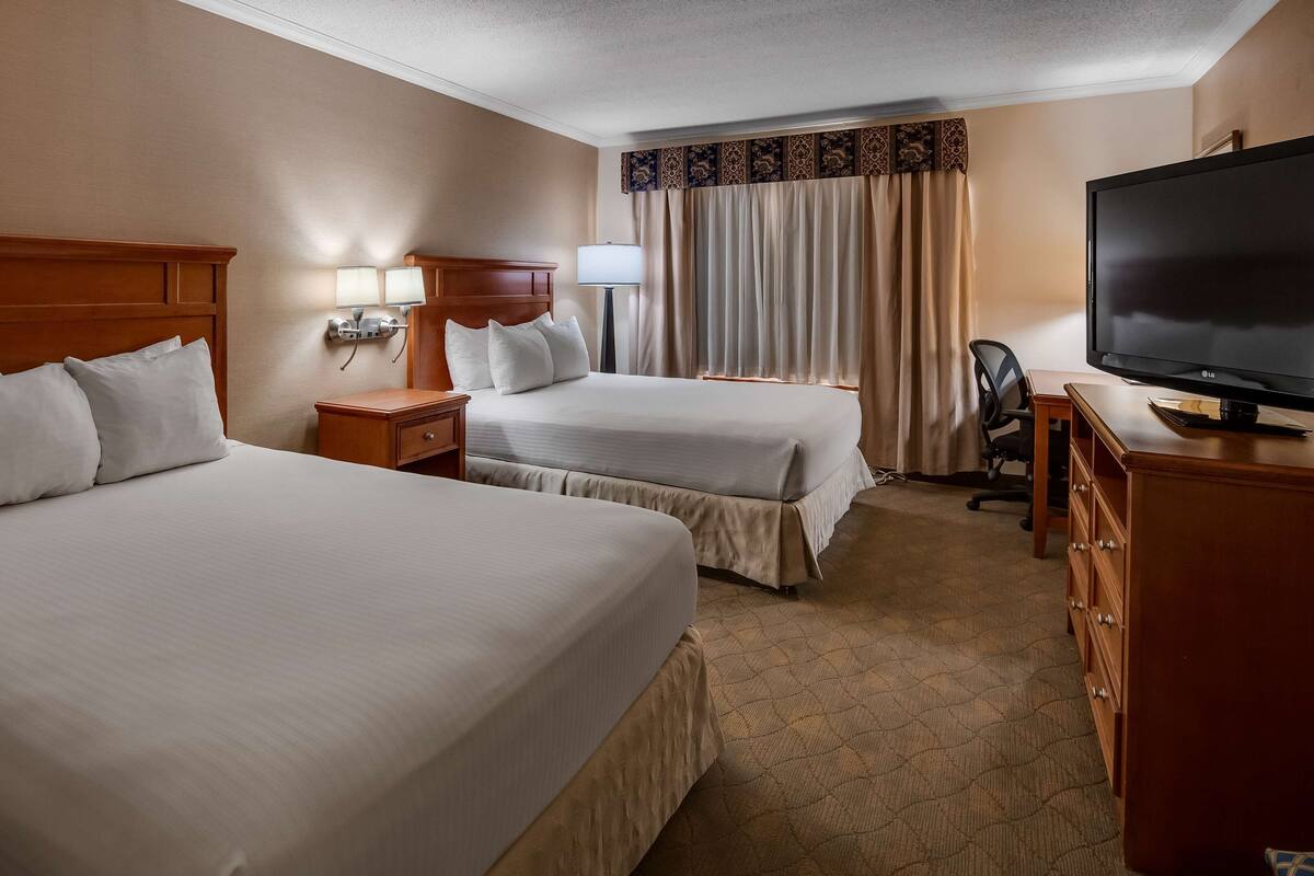 A hotel room with two beds, a TV, a desk, and a chair.