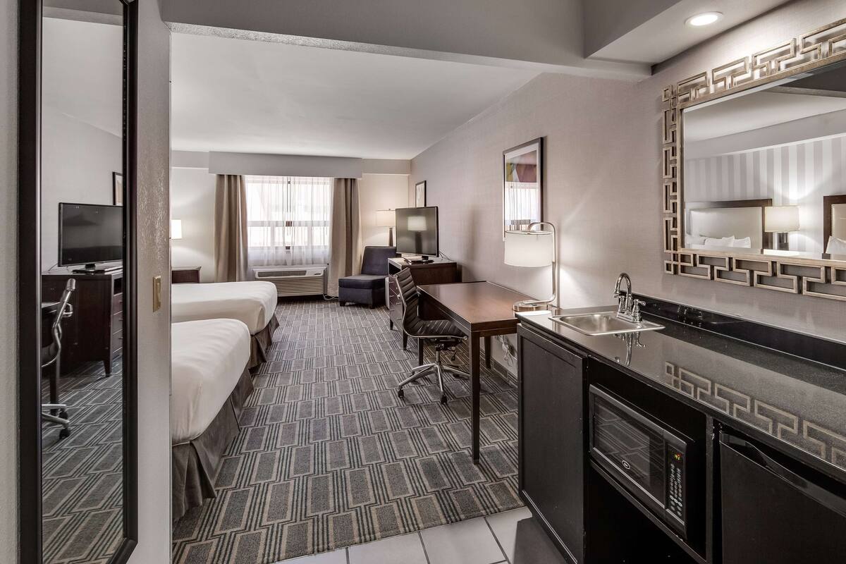 A hotel room with a bed, desk, chair, and kitchenette.