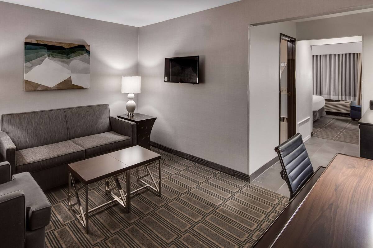 A hotel room with a sofa, two side tables with lamps, a flat-screen TV, and a patterned carpet.
