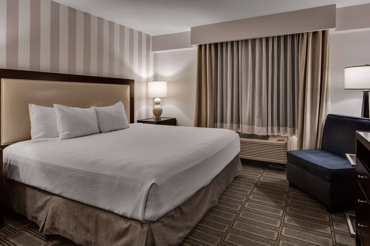 A hotel room with a large bed, a desk with a chair, a TV, and a window with curtains.