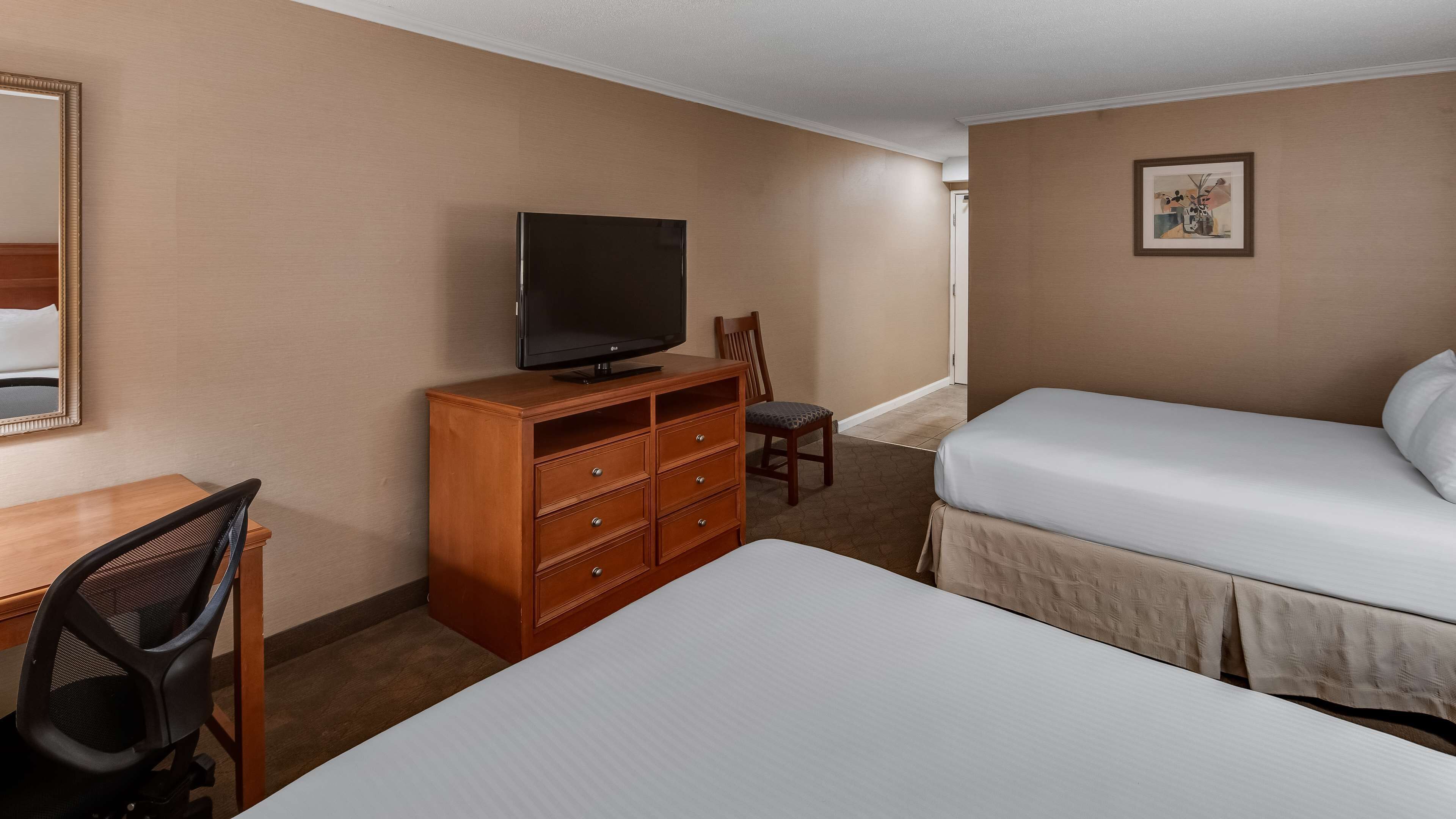 A hotel room with a bed, a TV on a wooden dresser, a chair, and a desk.
