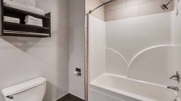 Une salle de bain équipée de toilettes, d’une douche et d’une étagère où sont rangées les serviettes.