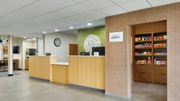 A hotel reception area with a wooden reception desk, a clock on the wall, a sign for Marriott Bonvoy, and a snack shelf.