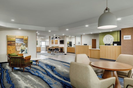 A hotel lobby with a reception desk, seating area, and artwork on the walls.. Fairfield Inn Ponca City