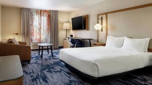 Ein Hotelzimmer mit Bett, Schreibtisch, Sessel, Sofa, Fernseher und einem Fenster mit Vorhängen.