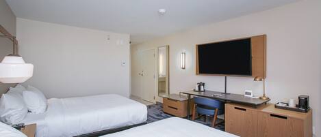 A hotel room with two beds, a desk with a chair, a coffee maker, and a flat-screen TV mounted on the wall.