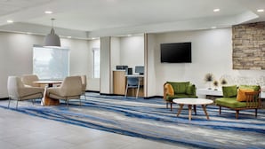 Eine moderne Hotellobby mit einem runden Tisch, zwei Sesseln, einer Couch, einem Flachbildfernseher, einer Wand mit Steinverkleidung und einem großen Fenster.