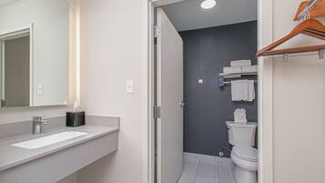 Un baño moderno con lavamanos, espejo y zona de ducha blancos.
