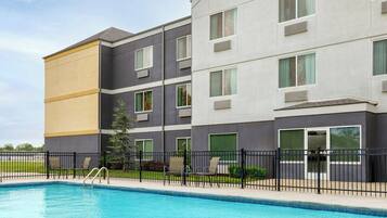 Un hotel de varios pisos con piscina, mobiliario exterior y un patio cercado.