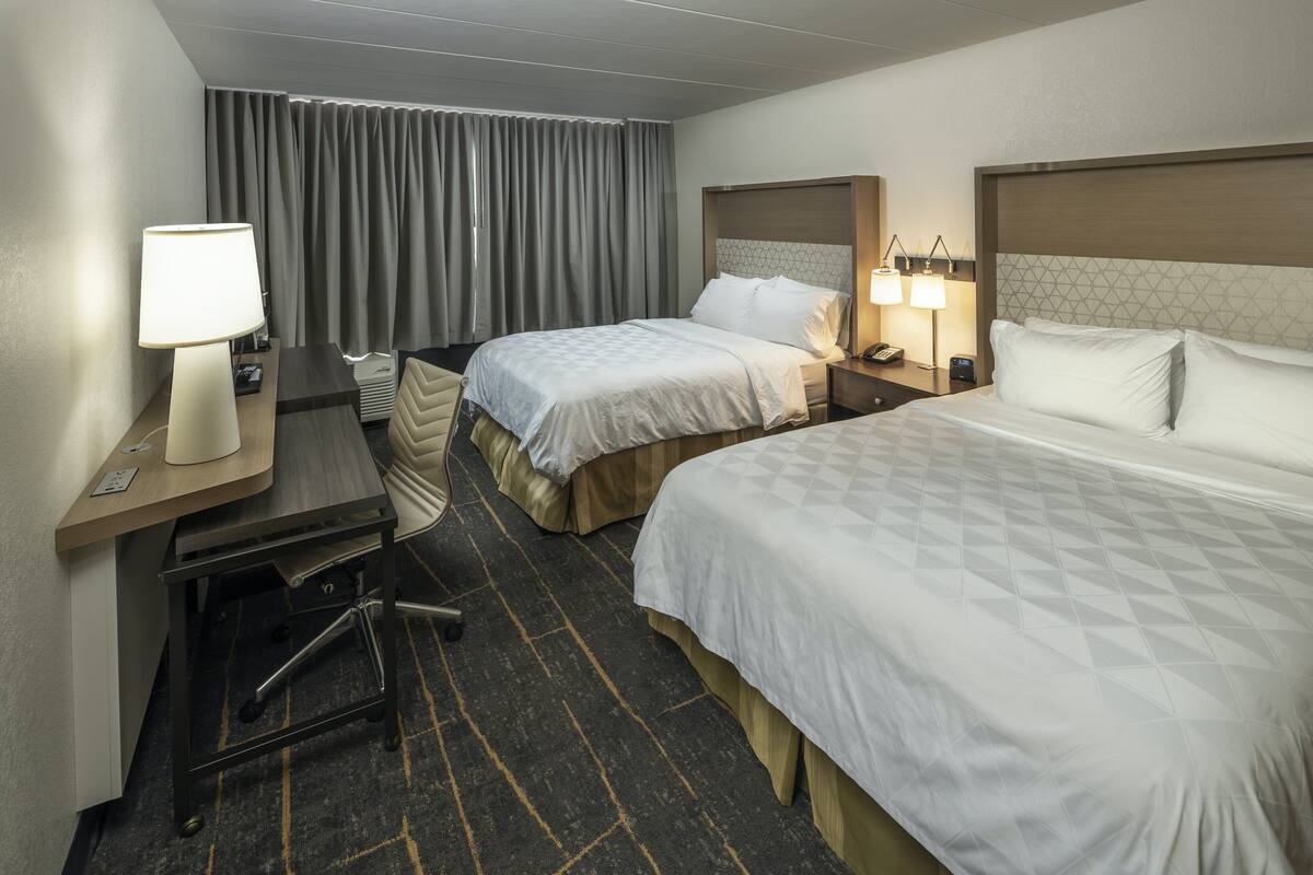 A hotel room with two beds, a desk with a lamp, a chair, and a small table.