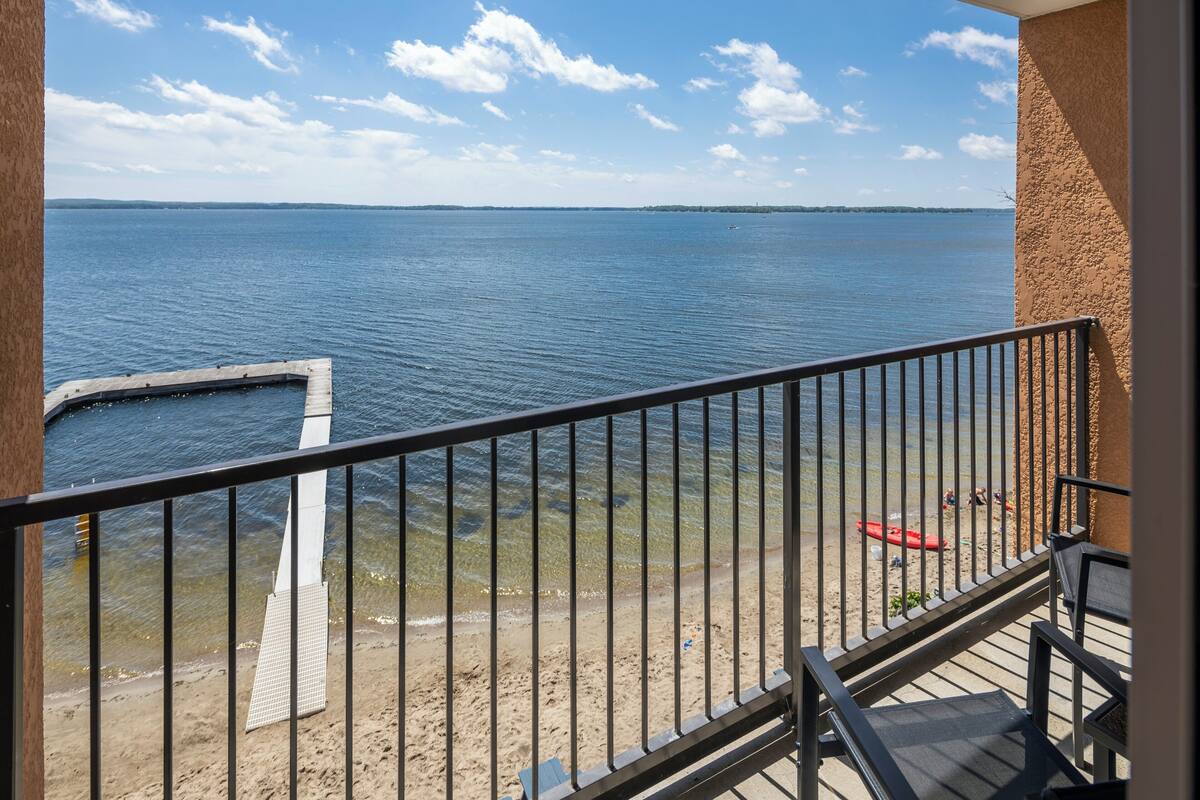 A balcony with a view of a calm body of water, a sandy beach, and a distant shoreline.