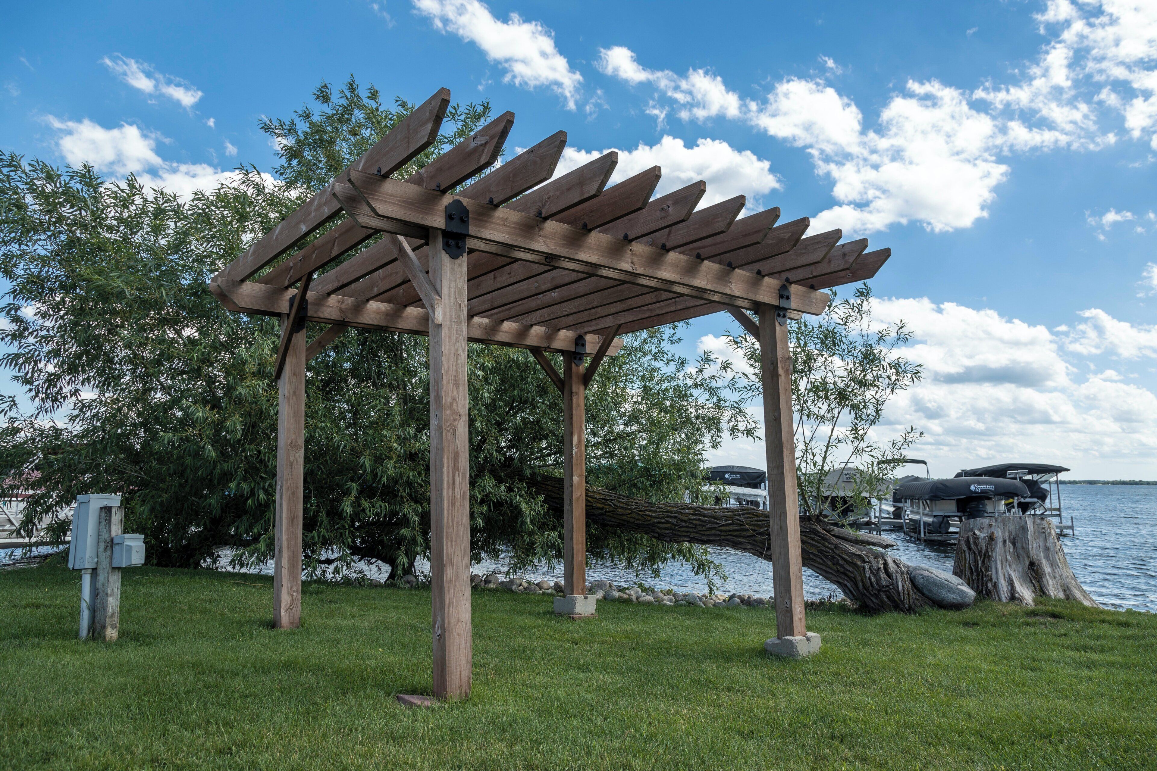Et pergola af træ med udsigt over en sø og både i baggrunden.