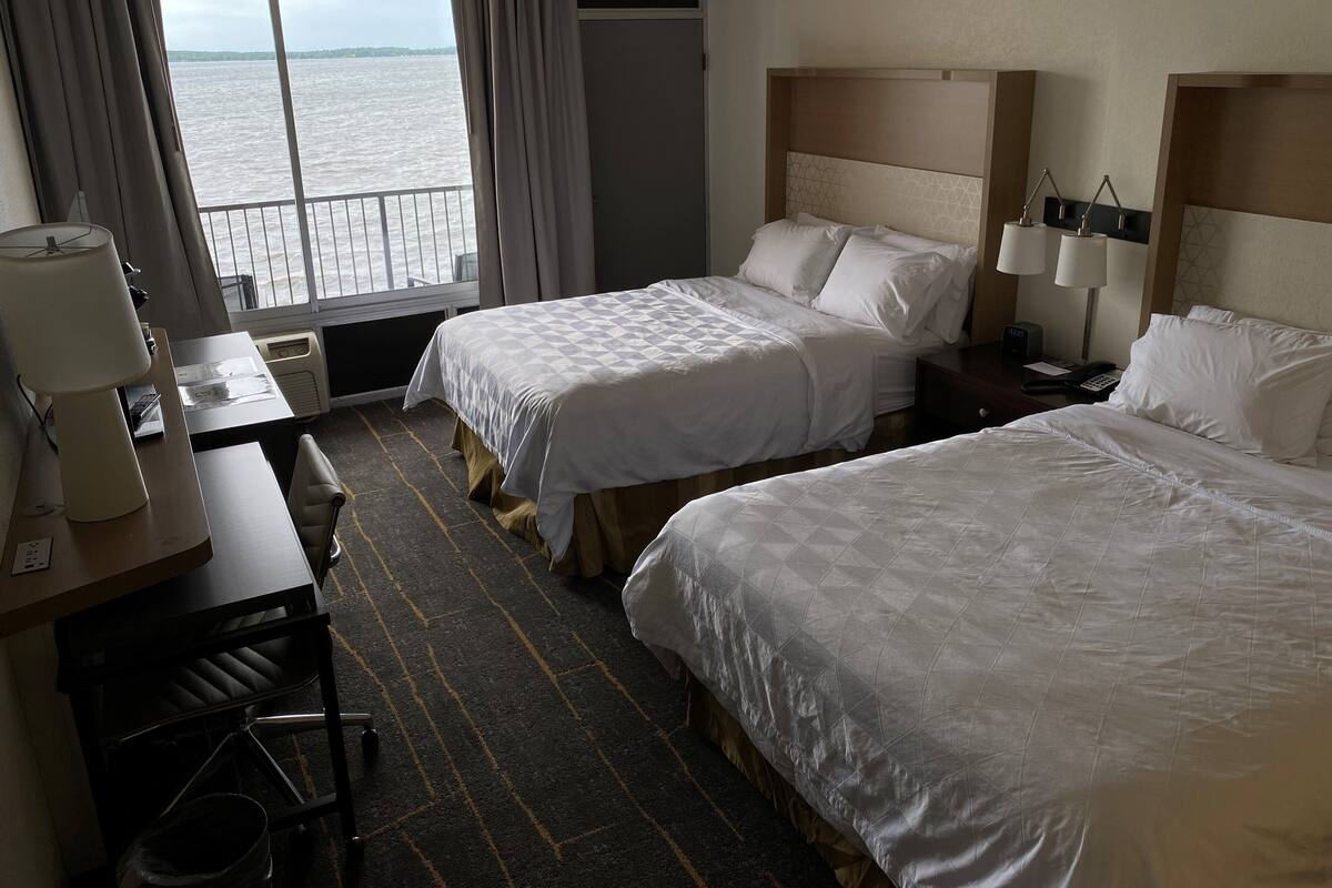 A hotel room with two beds, a desk, a chair, a lamp, and a view of the water.