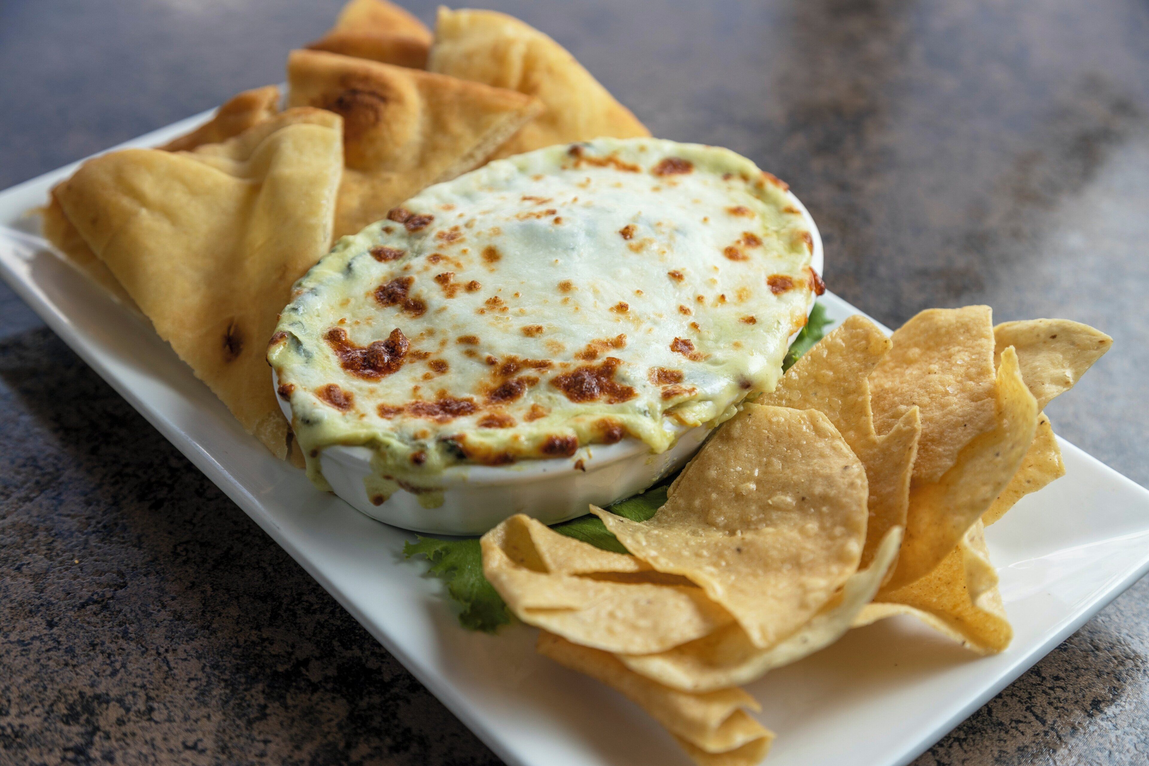 A white plate with a baked dish, tortilla chips, and a green leafy garnish.