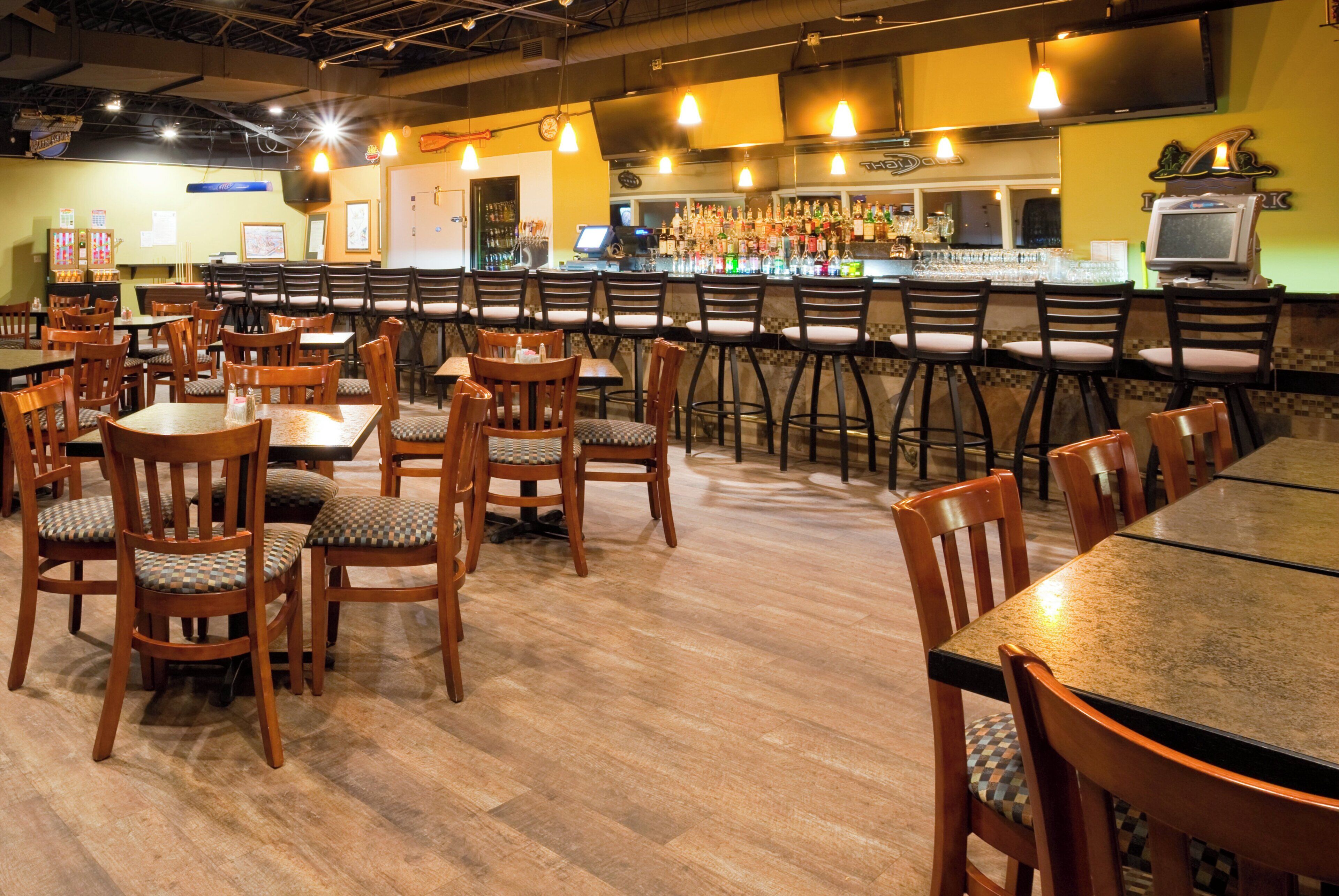 A restaurant interior with multiple tables and chairs, a bar area with various bottles, and a television screen.
