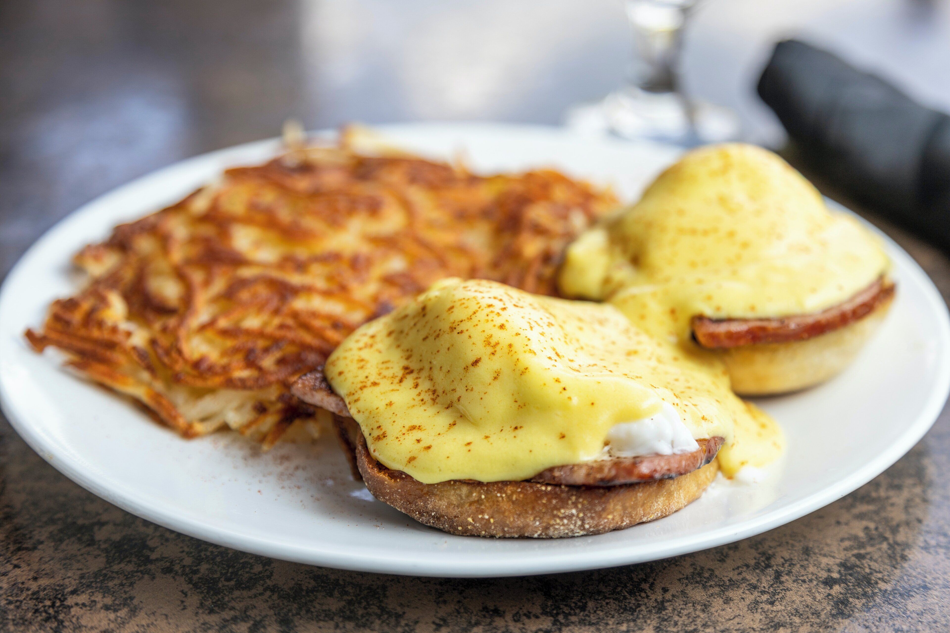 A plate with two eggs benedict sandwiches and a side of hash browns.