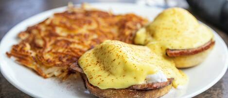 A plate with two eggs benedict sandwiches and a side of hash browns.