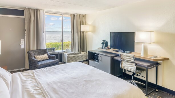Quarto de hotel com cama, escrivaninha com cadeira, televisão e janela com vista para a água.