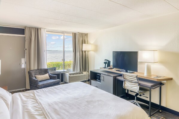 Una habitación de hotel con una cama, un escritorio con una silla, un televisor y una ventana con vista al agua.
