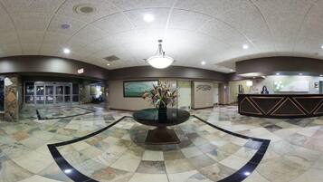 A lobby with a central round table, a reception desk, and a stone pillar.