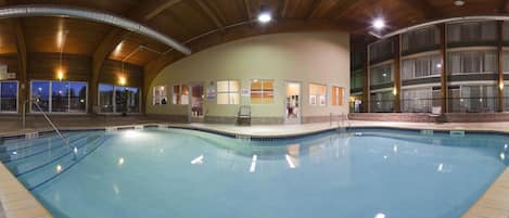 An indoor swimming pool with a wooden ceiling and a view of the outside at dusk.