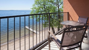 A balcony with a view of the water, a table, and two chairs.