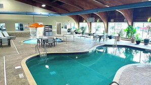 Piscina interna com água cristalina, rodeada por espreguiçadeiras, mesas e plantas em vasos.