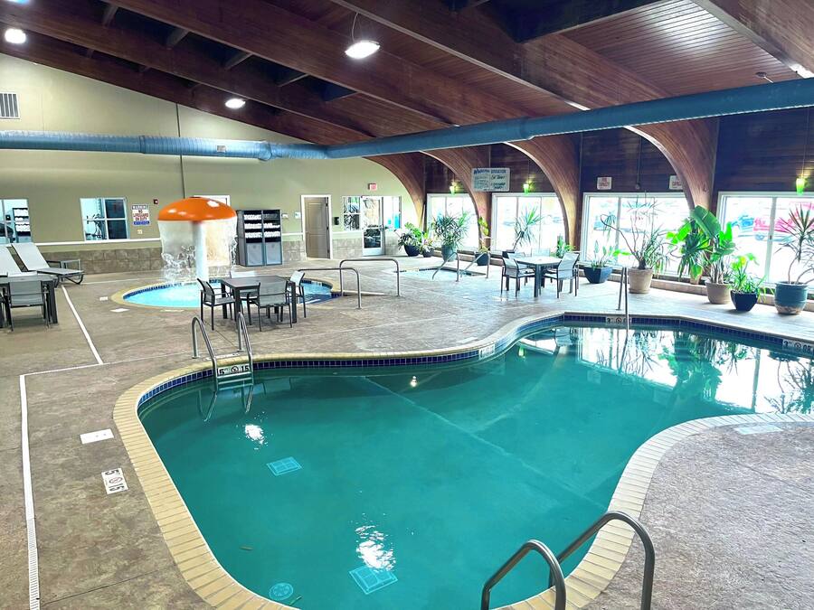 An indoor swimming pool with clear water, surrounded by lounge chairs and tables, and potted plants.