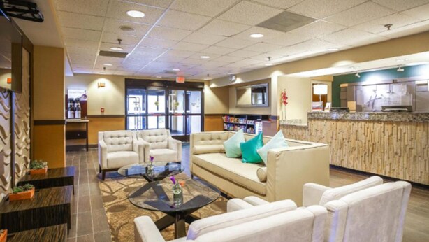 Eine Hotelhalle mit Rezeption, einer Sitzecke mit Sofas und Sesseln, einem Couchtisch und einem Fernseher.
