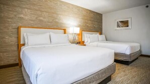 Ein Hotelzimmer mit zwei Betten, Holz-Kopfteilen, weißer Bettwäsche, einem Nachttisch mit Lampe und einem gerahmten Bild an der Wand.