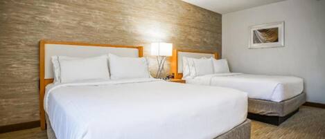 Habitación de hotel con dos camas, cabeceros de madera, ropa de cama blanca, una mesita de noche con lámpara y un cuadro en la pared.
