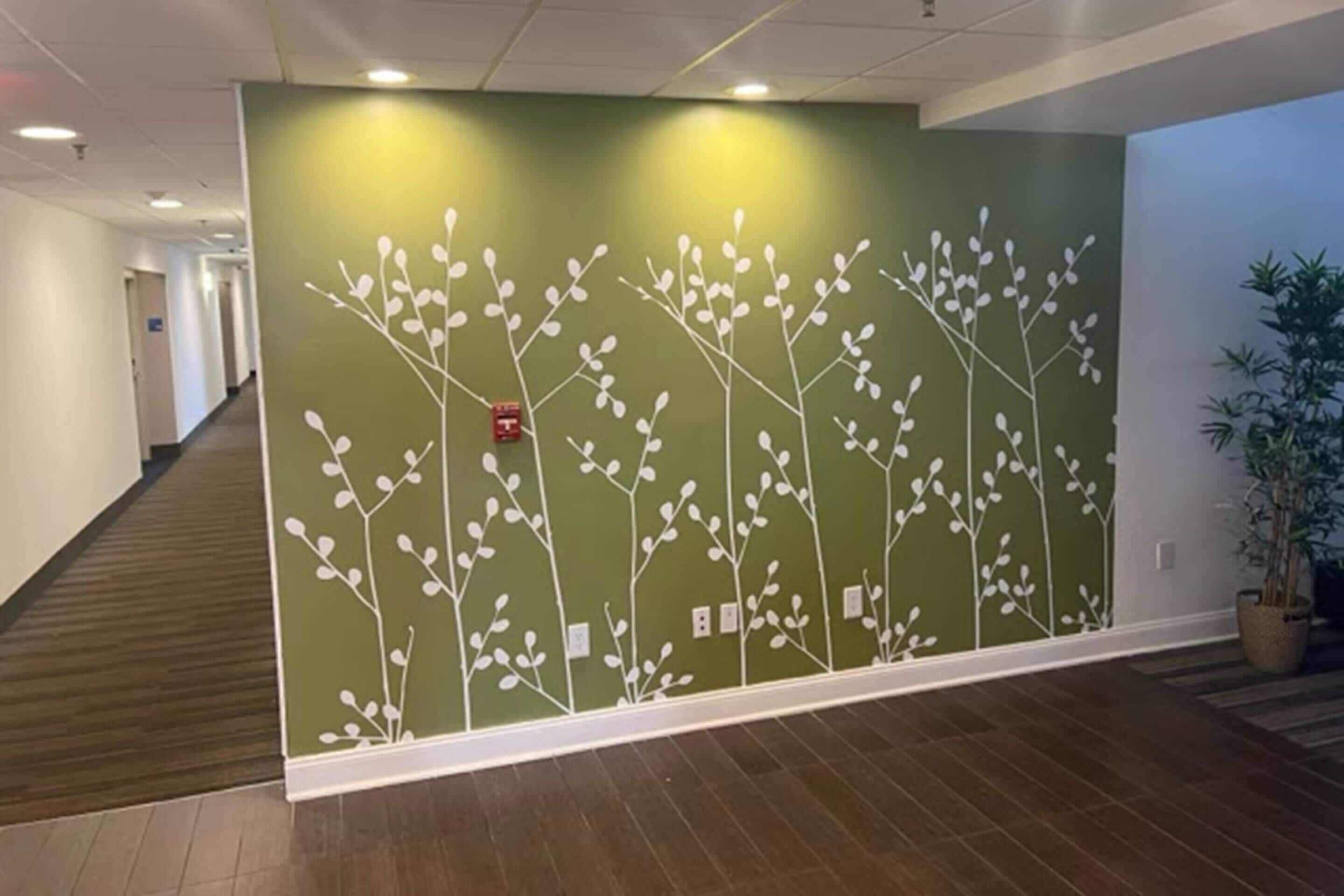 Un couloir avec un mur vert orné d’un motif d’arbre blanc, un plancher en bois et une plante en pot.