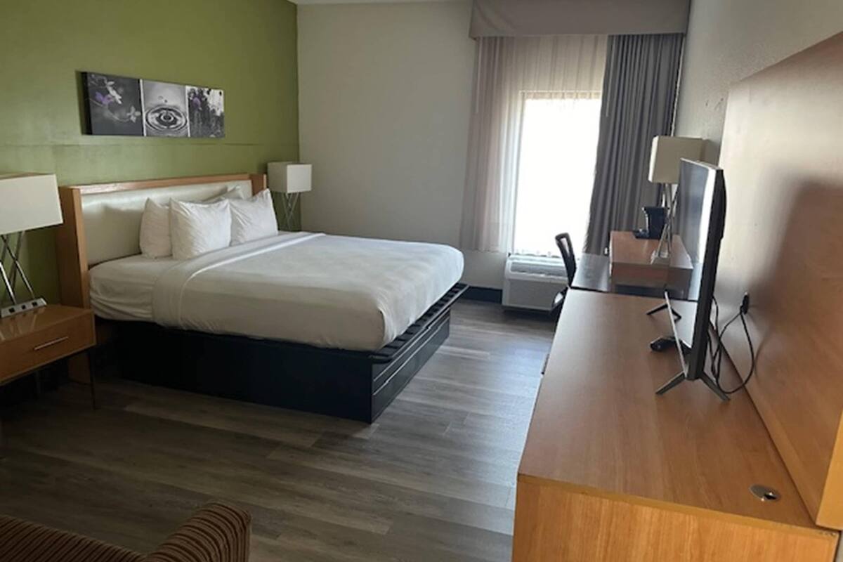 Habitació d'hotel amb un llit, taules de nit, escriptori, cadira i finestra amb cortines.