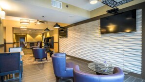 Eine Lobby mit modernem Design, inklusive einer strukturierten Wand, einem Flachbildfernseher und Sitzbereichen mit Stühlen und einem kleinen Tisch.