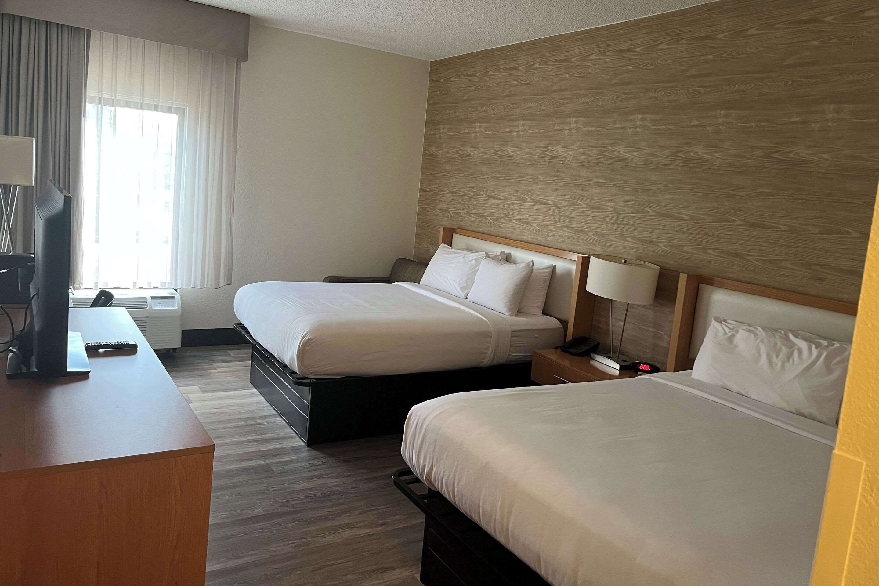 Una habitación de hotel con dos camas, un escritorio, una lámpara y una ventana con cortinas.