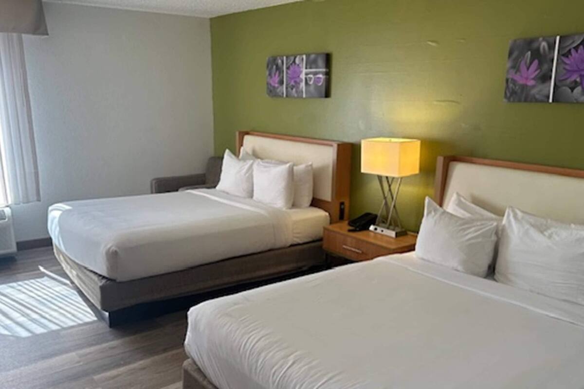 Habitació d'hotel amb dos llits, una tauleta de nit amb una làmpada i obres d'art a les parets.