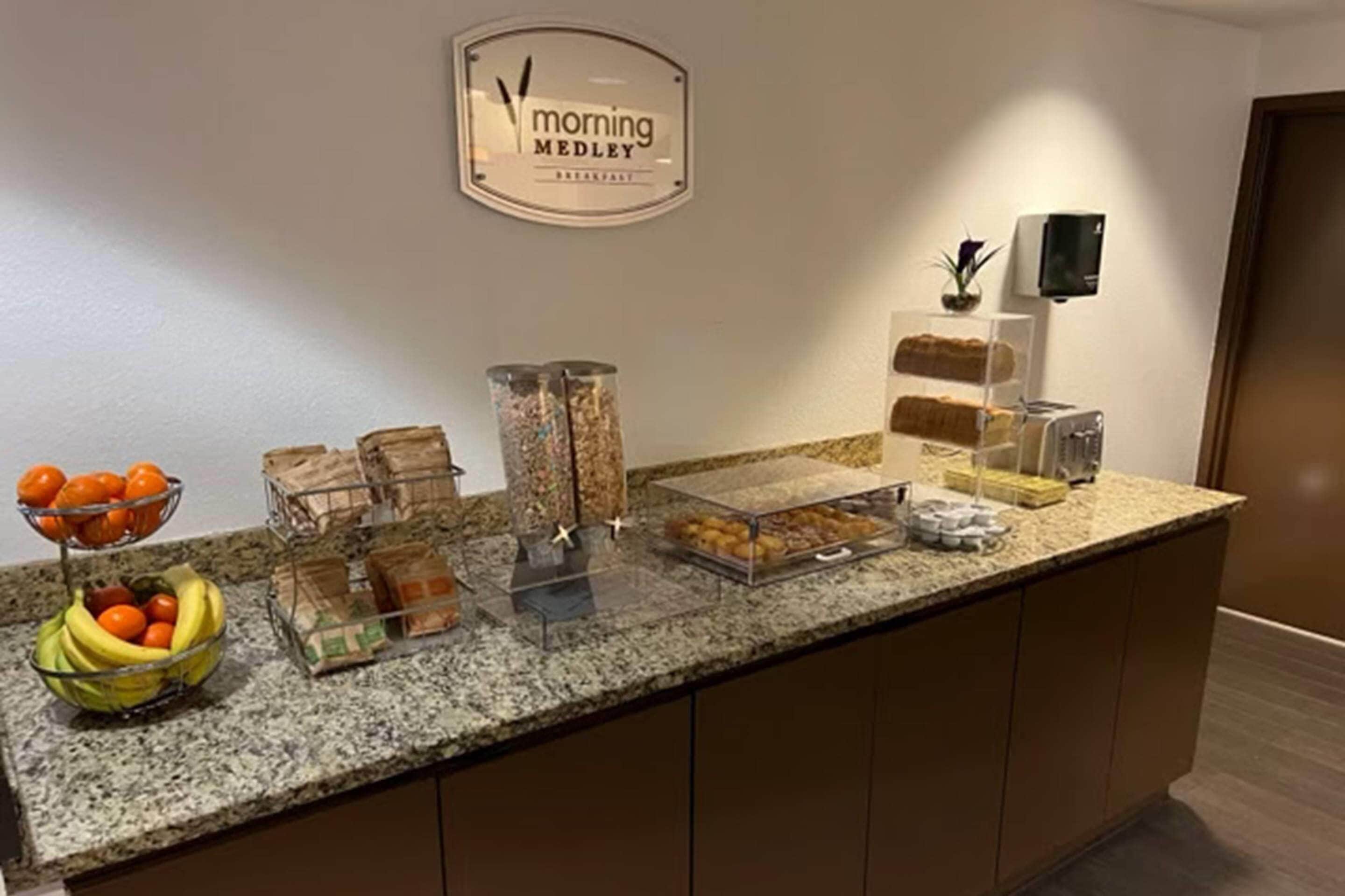 Een ontbijtbuffet met diverse soorten eten, een bord met de tekst 'Morning Medley Breakfast' en een koffieapparaat.